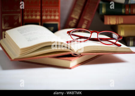 Stack of books with red women's glasses placed on the open book on the white background with copy space Stock Photo