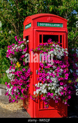 Flower covered disused telephone box now contains defribillator Stock Photo