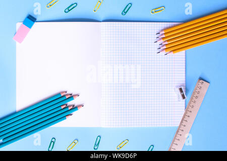 Notebook in a cage with a pencils, eraser, ruler, paper clips and other office supplies on a blue background. Concept back to school. Place for text. Stock Photo