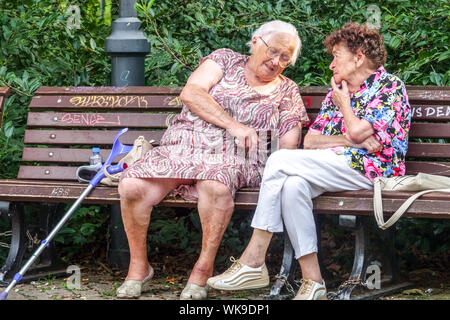 Two senior women sitting on a park bench, elderly people seniors talking Stock Photo