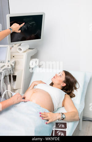 Sonographer pointing to a specific point on fetus sonogram dislpayed on ultrasound scanner monitor  during obstetric or pregnancy ultrasonography proc Stock Photo