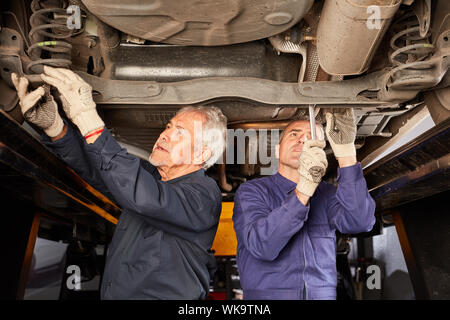 Two mechanics repairing or inspecting a car on the lift Stock Photo