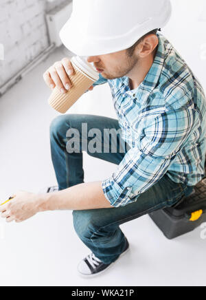 architect and home renovation concept - builder sitting on toolkit and drinking take away coffee Stock Photo