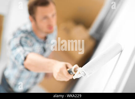 interior design and home renovation concept - man colouring the wall with roller Stock Photo