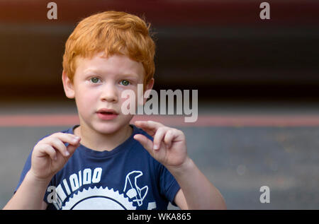 Portrait European boy with green eyes. Child with curly ginger hair. Talking with sign language. Boy talking nonverbal. Hearing loss. Deaf disability
