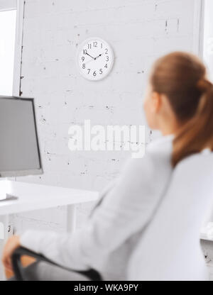 business, office, school and education concept - businesswoman looking at wall clock in office Stock Photo