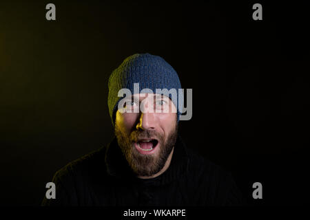 handsome modern caucasian man in blue wool hat and black sweater shouting with opened mouth with emotions Stock Photo