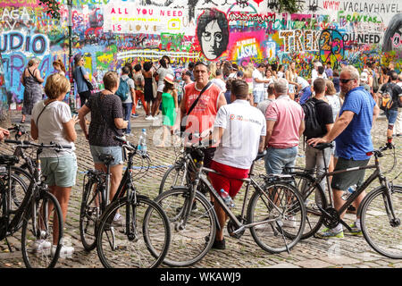 Crowds of people Prague tourists and a group of people city bikers stopped in front of the John Lennon Wall Prague tour Czech Republic Stock Photo