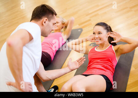 fitness, sport, training, gym and lifestyle concept - group of smiling women with male trainer doing sit ups on mats in the gym Stock Photo