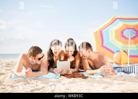 group of smiling people with tablet pc on beach Stock Photo