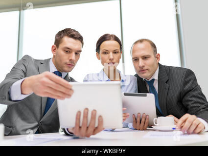 business, technology and office concept - serious business team with tablet pc computers, documents and coffee having discussion in office Stock Photo