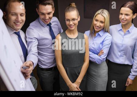 business and office concept - smiling business team with charts on flip board having discussion Stock Photo