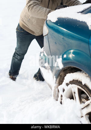 transportation, winter and vehicle concept - closeup of man pushing car stuck in snow Stock Photo