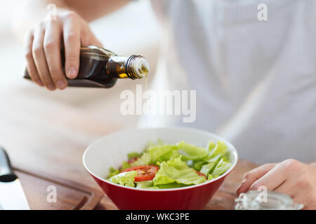 cooking and home concept - close up of male hands flavouring salad in a bowl with olive oil Stock Photo