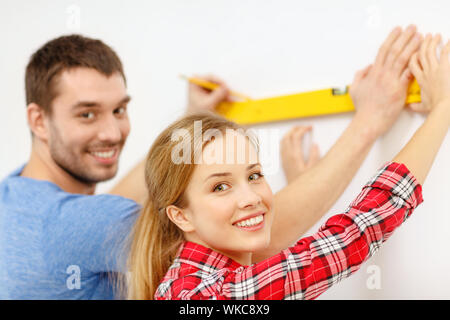 repair, building and home concept - smiling couple building new home using spirit level to measure Stock Photo