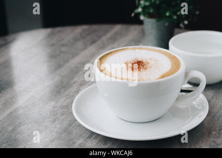 Hot coffee, hot tea  and flower vase with green leaves place on the marble table in early morning with copy space, white cup and silver spoon. Stock Photo