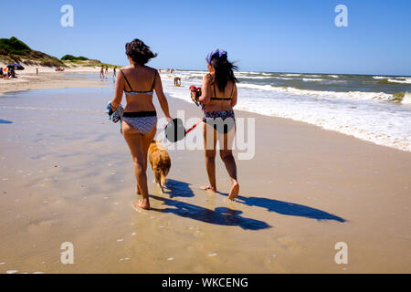 Uruguay: Uruguay, La Floresta, small city and resort on the Costa de Oro (Golden Coast). Two young woman wearing a swimsuit are walking their dog with Stock Photo