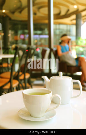 Vertical image of a white cup and teapot of green tea served on cafe's white table Stock Photo