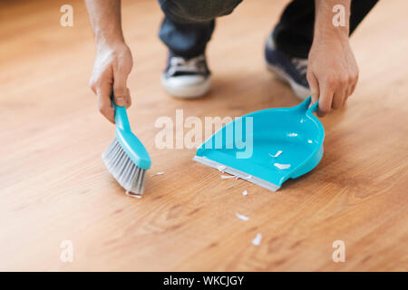 cleaning and home concept - close up of male brooming wooden floor with small whisk broom and dustpan Stock Photo