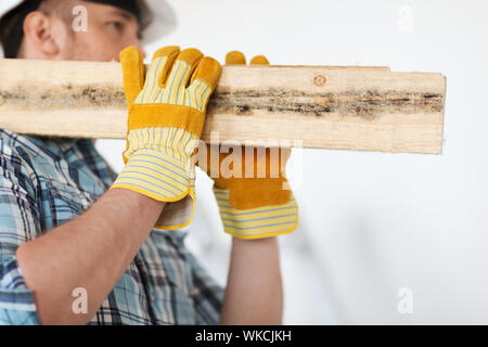 repair, building and home concept - close up of male in gloves and helmet carrying wooden boards on shoulder Stock Photo