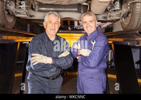 Two car mechanics with competence and experience in front of lift in the auto repair shop Stock Photo