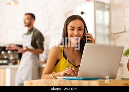 Sitting near laptop. Dark-haired successful female entrepreneur sitting near laptop while ordering foods Stock Photo
