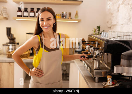 Coffee time. Beautiful dark-eyed woman feeling good while making coffee for clients Stock Photo
