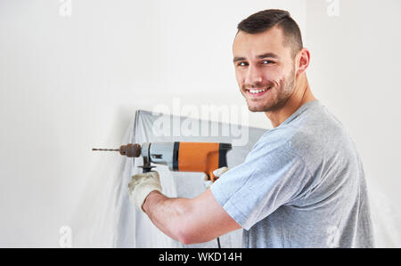 Young man as a handyman with drill while drilling a hole in the wall Stock Photo