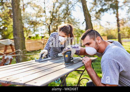 Couple doing home improvement in the garden with grinder while grinding off a wooden table Stock Photo