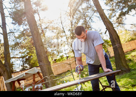 Young man at garden furniture prime and paint as home improvement work in summer Stock Photo