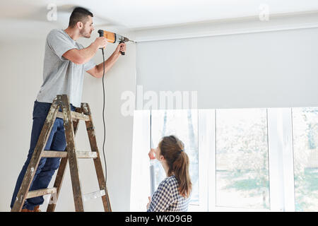 Young couple as a home improvement during the installation of a window roller blind while renovating Stock Photo