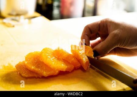 closeup of a woman cutting an orange in slices in a professional kitchen Stock Photo