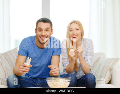 food, love, family, sports, entretainment and happiness concept - smiling couple with popcorn cheering sports team at home Stock Photo