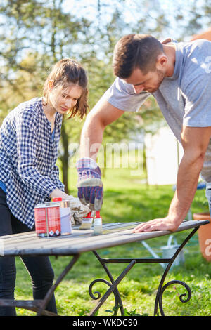 Young couple as a home improvement paints and renovates together a table in the garden in summer Stock Photo