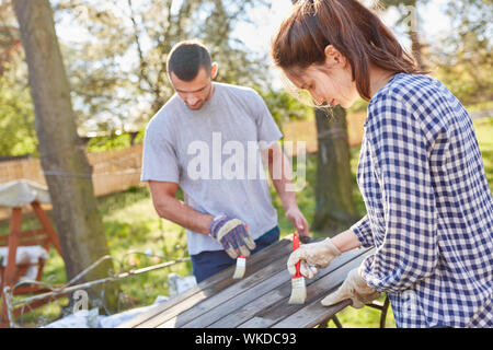 Handyman couple together paint a table in the garden in the summer as a protective coat Stock Photo