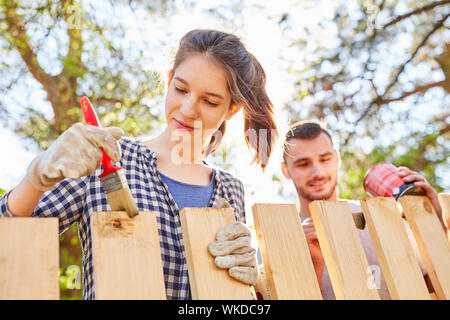 Young woman and friend together in priming and varnishing wooden fence in the garden Stock Photo