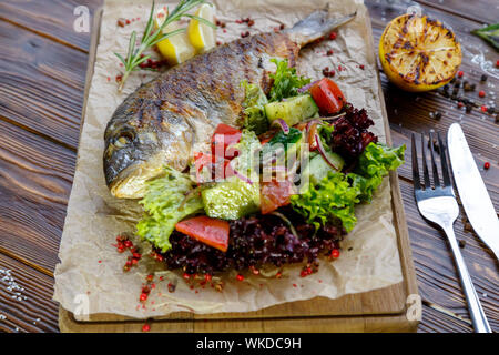 Grilled fish with vegetables and herbs on the kitchen board on a brown wooden background Stock Photo