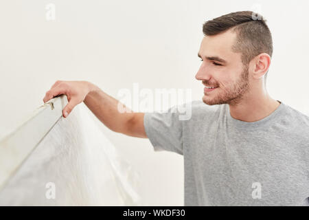 Young handyman with spirit level on wall at the renovation of a new apartment Stock Photo