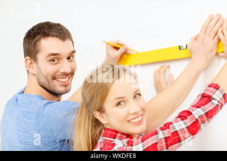 repair, building and home concept - smiling couple building new home using spirit level to measure Stock Photo