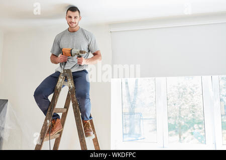 Young man as a home improvement with drill sits on a ladder at the home renovation