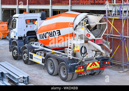 London construction building site Euromix delivery mixer lorry truck loaded with ready mix cement concrete reversing beside scaffolding England UK Stock Photo