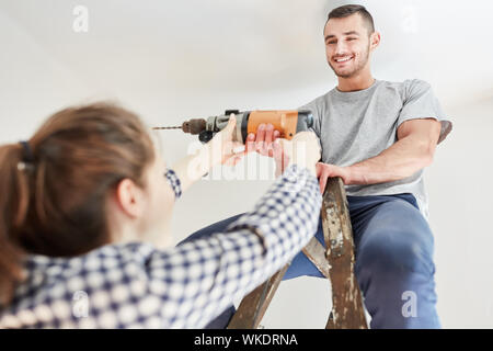 Young couple using drill while renovating apartment or house in teamwork Stock Photo