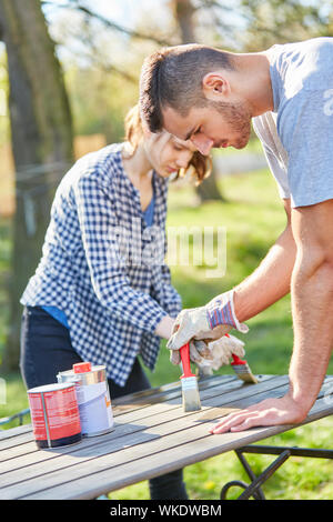 Handyman couple in the garden while painting the furniture with brush and protective paint Stock Photo