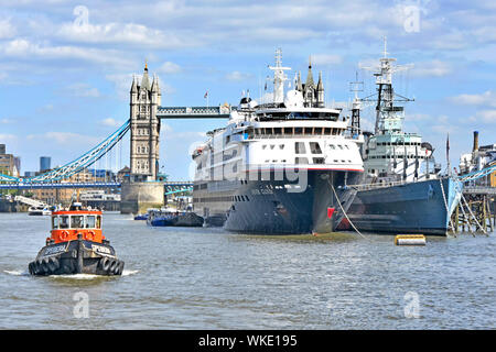 River Thames tug boat passes cruise ship liner Silver Cloud docked beside warship HMS Belfast imperial war museum with iconic Tower Bridge London UK Stock Photo