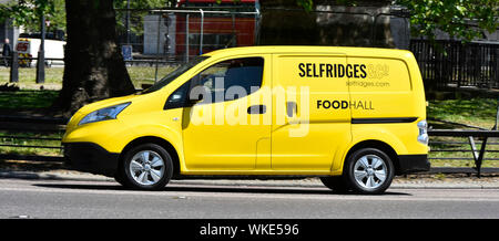 Side view of yellow Selfridges & Co department store delivery van with driver from Food Hall at work driving along Park Lane Mayfair London England UK Stock Photo