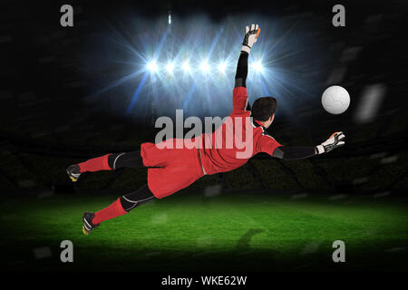 Fit goal keeper jumping up against football pitch under spotlights Stock Photo
