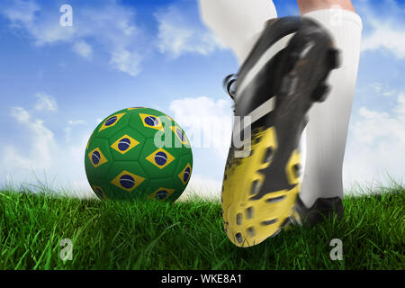 Composite image of football boot kicking brasil ball against field of grass under blue sky Stock Photo