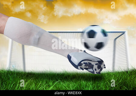 Composite image of close up of football player kicking ball against goalpost on grass under yellow sky Stock Photo