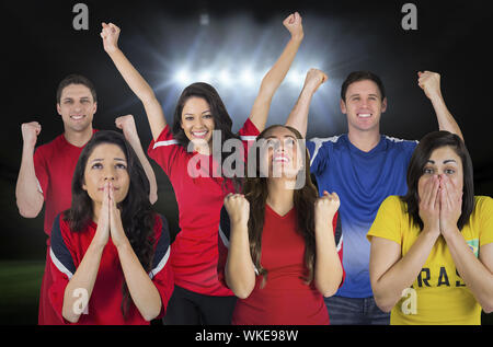 Composite image of various football fans against football pitch under spotlights Stock Photo