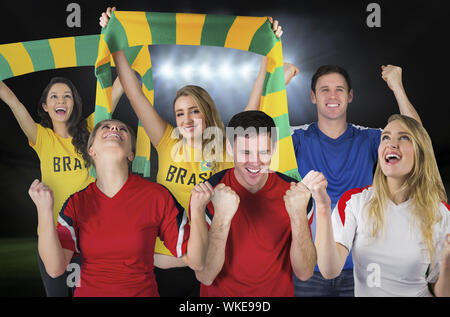 Composite image of various football fans against football pitch under spotlights Stock Photo